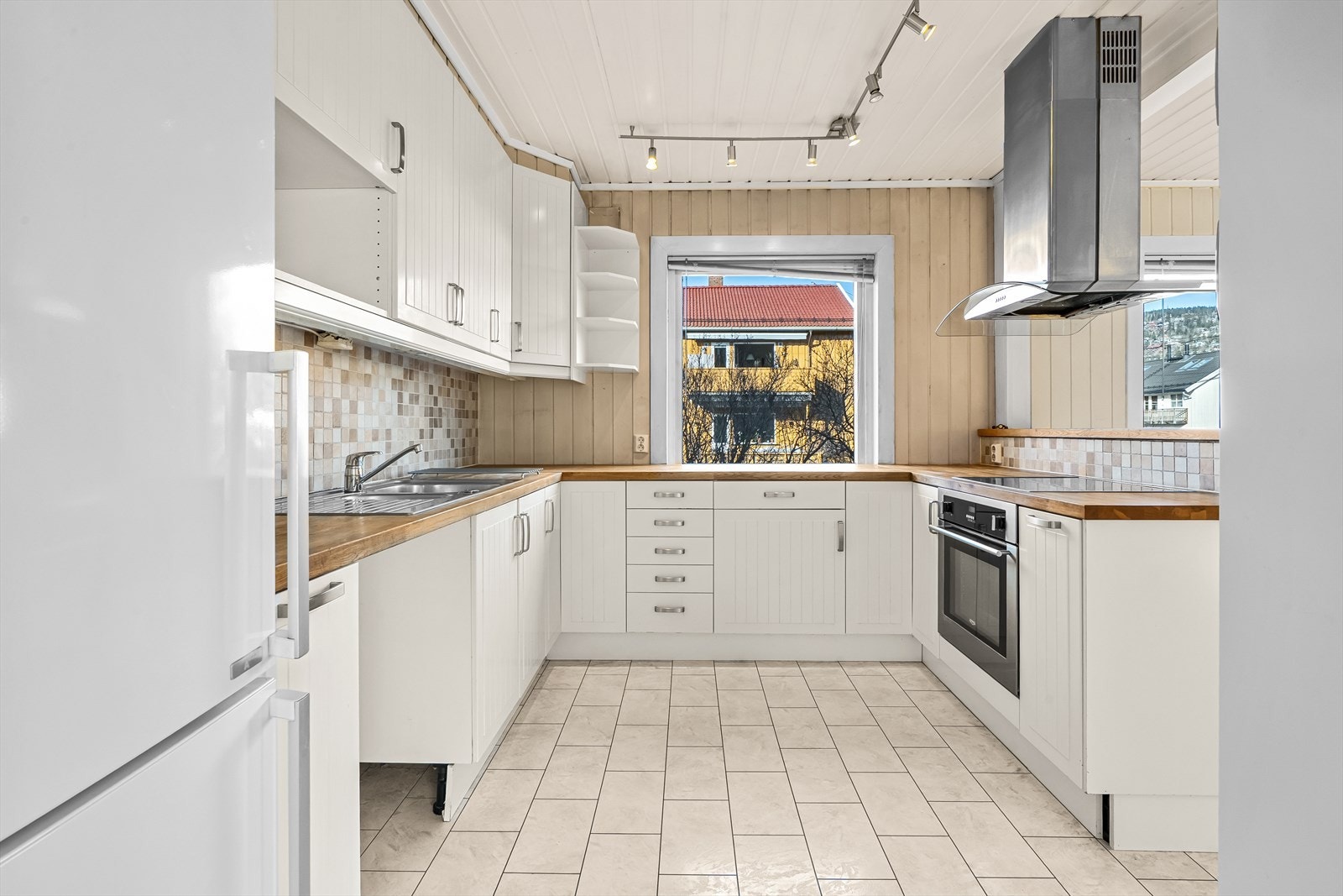 Kjøkken med lyse profilerte fronter og heltre benkeplate, utstyrt med frittstående kjøl/fryseskap, integrert platetopp, stekeovn og avtrekksvifte. Galleribilde