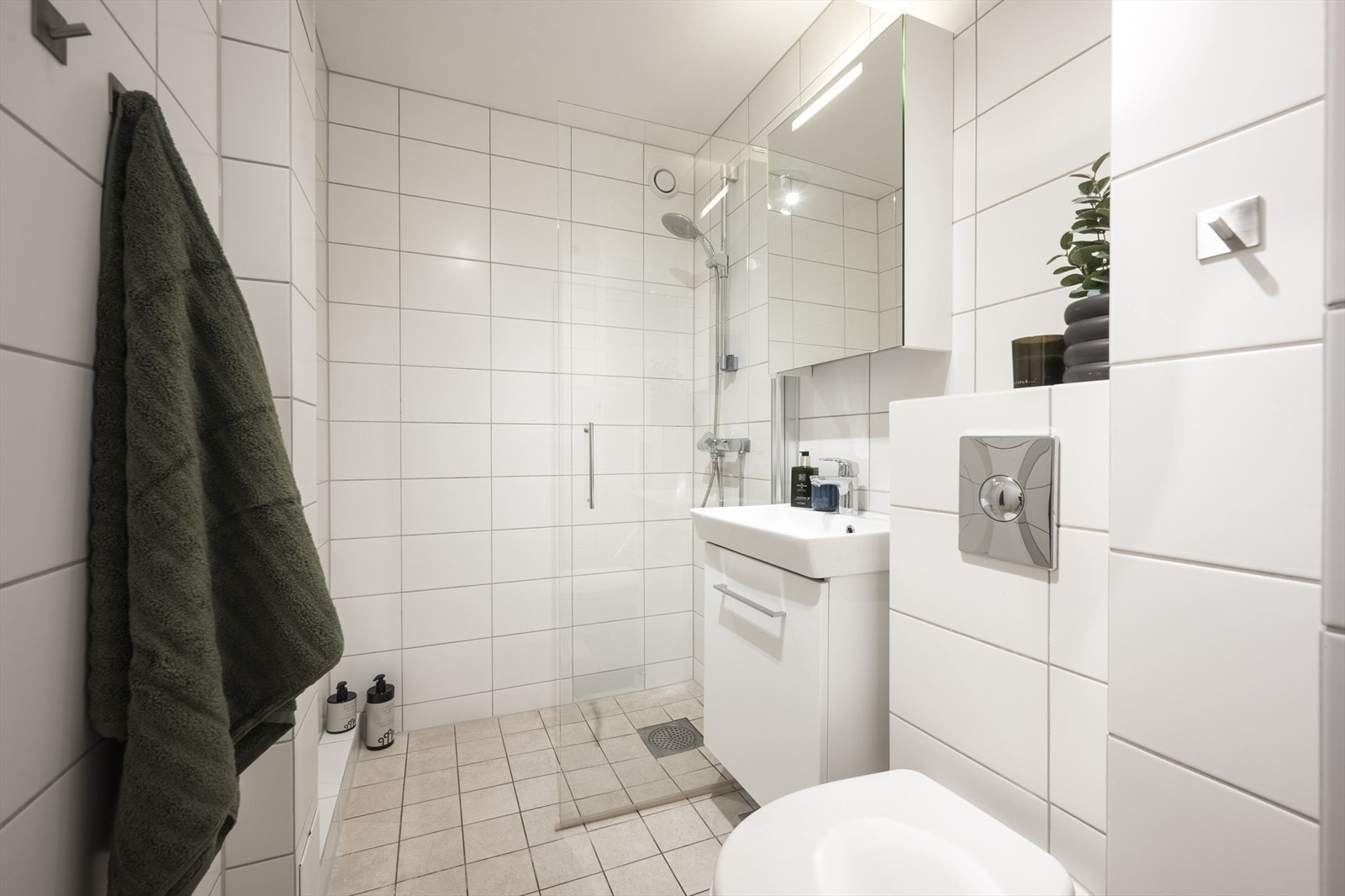 Badet inneholder vegghengt toalett, dusjnisje med glassvegg og baderomsinnredning med skap, servant, ett-greps blandebatteri og speilskap. Galleribilde