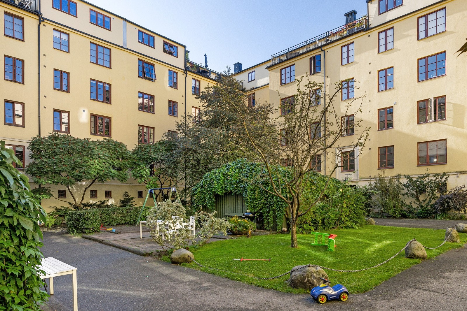 Pent opparbeidet gårdsrom med asfaltert adkomst, plen, beplanting, trær og sittegrupper Galleribilde