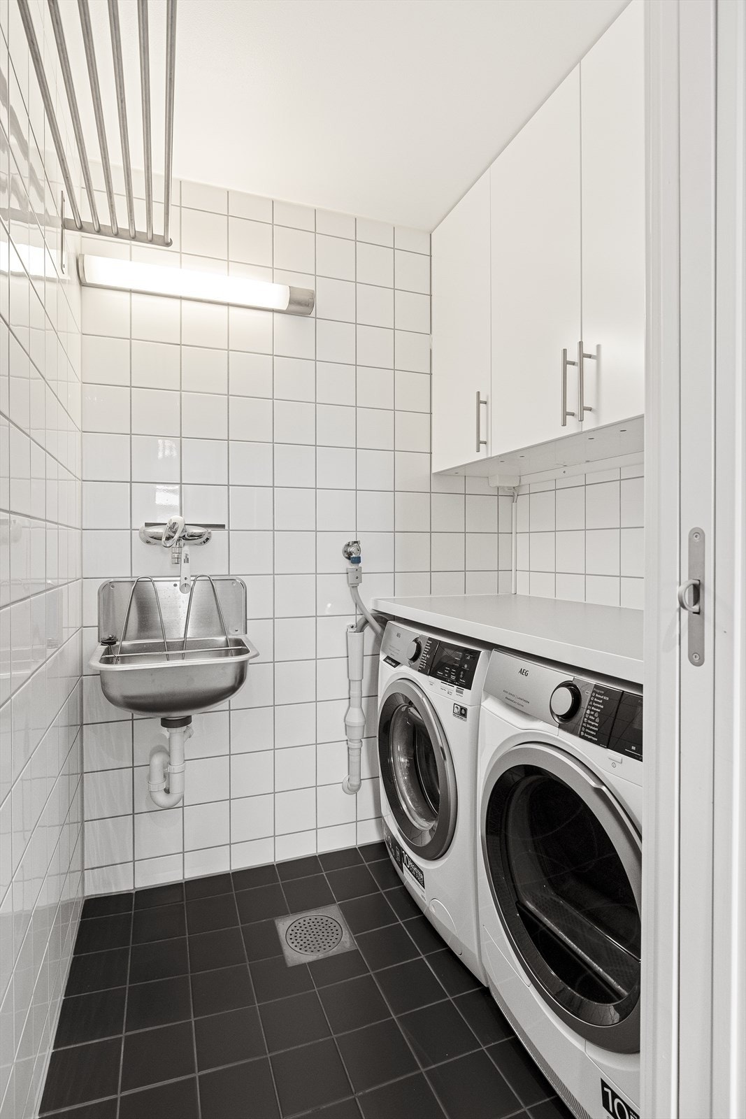 Meget praktisk vaskerom i tilknytning til bad er flislagt, med plass til vaskemaskin og tørketrommel. Innredning med benkeplate og vegghengte skap. Utslagsvask Galleribilde
