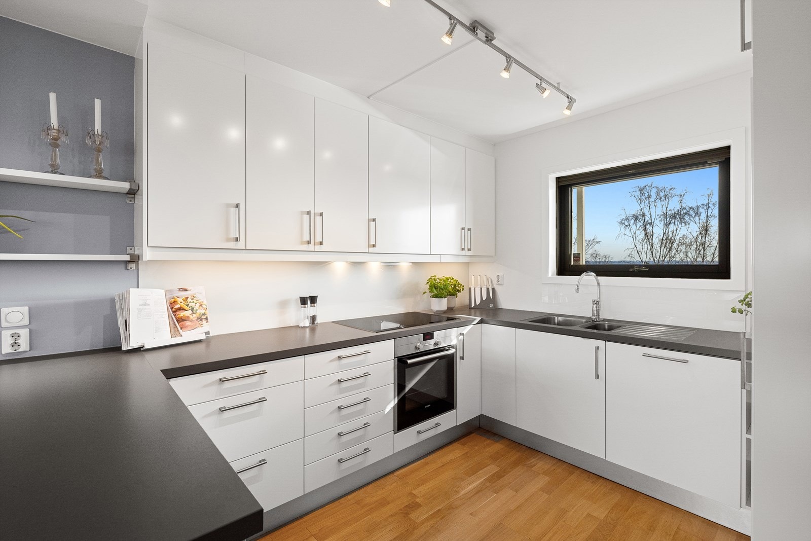 Kjøkkeninnredningen er spesialtilpasset leiligheten, og har lyse slette fronter, 4 cm. bred lys grå laminert benkeplate, og plateslått backsplash Galleribilde