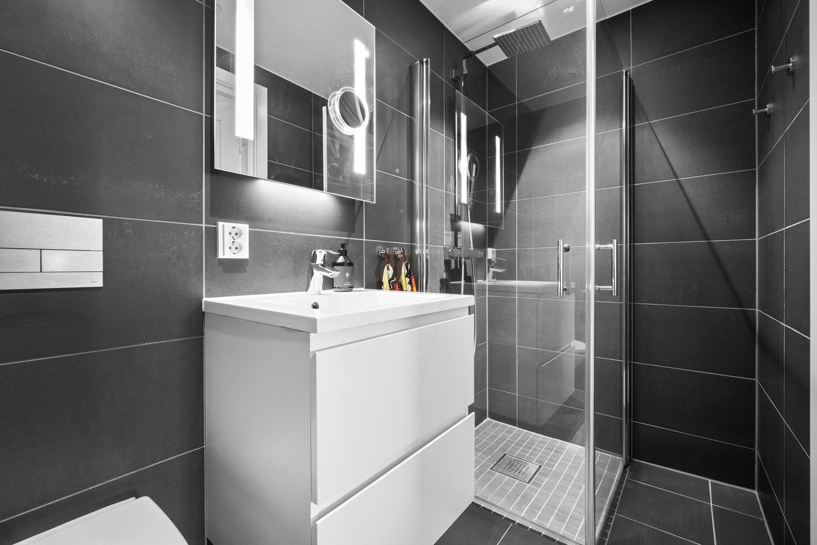 Delikat og innbydende bad med dusjdører i herdet glass, servant med underskap og vegghengt klosett. Gulvvarme og downlights Galleribilde