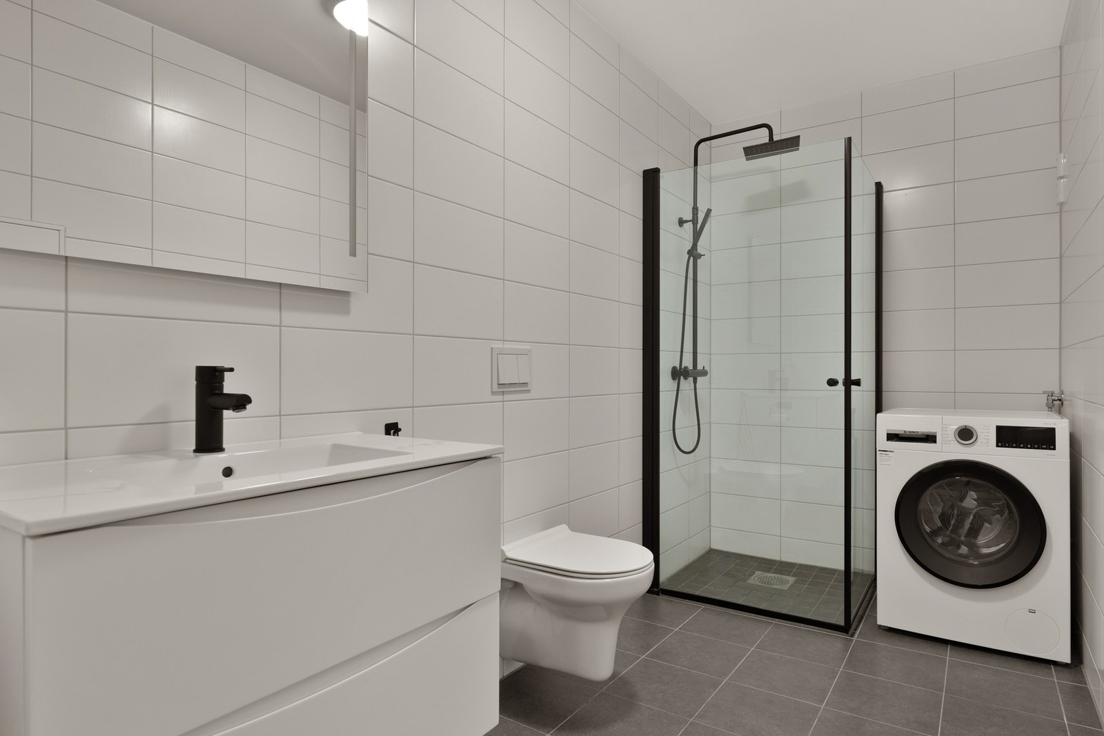 Bad/vaskerom med nedfelt sevant, veggheng toalett og dusjhjørne samt opplegg for vaskemaskin. Galleribilde