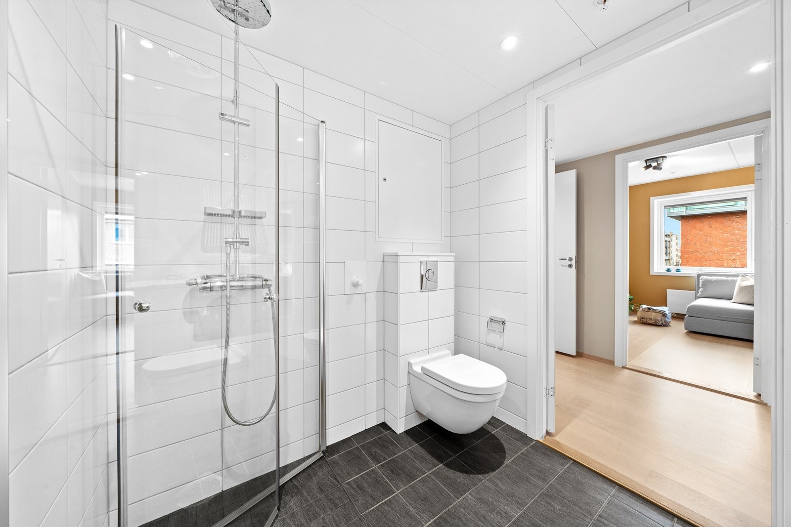 Baderomsinnredningen består av vegghengt toalett, servant med underskap og benkeplate, stor speilflate og dusjhjørne med innfellbare glassdører. Galleribilde