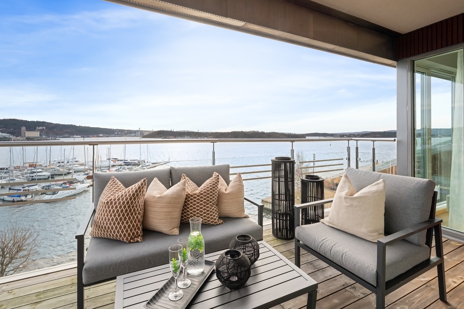Balkongen har dekke av terrassebord, overbygg på sjøsiden og glassrekkverk på begge sider for uhindret sikt. Galleribilde