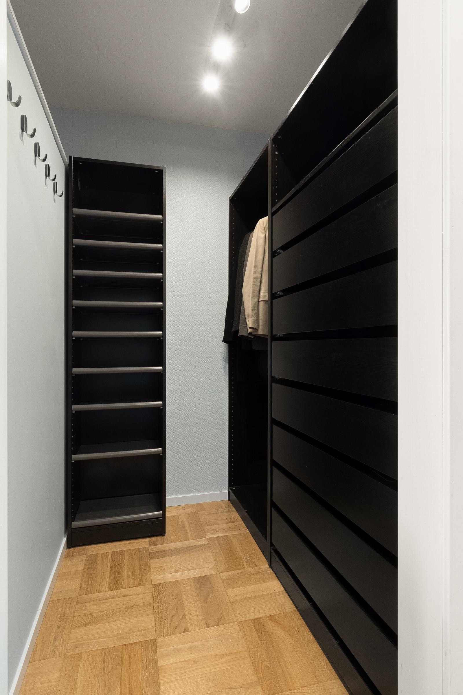 Effektiv og stilfull walk-in garderobe med sort innredning for oppheng av klær og skuffer for oppbevaring. Galleribilde