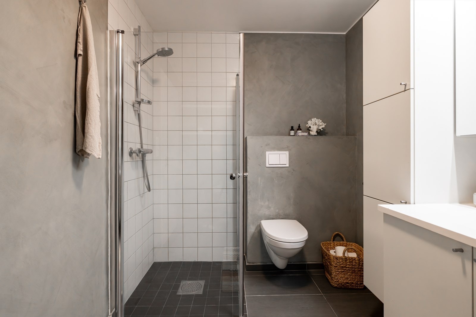 Badet er innredet med servant i skuffeseksjon og høyskap for oppbevaring. Videre er det vegghengt toalett og dusjhjørne med innfellbare glassdører. Galleribilde