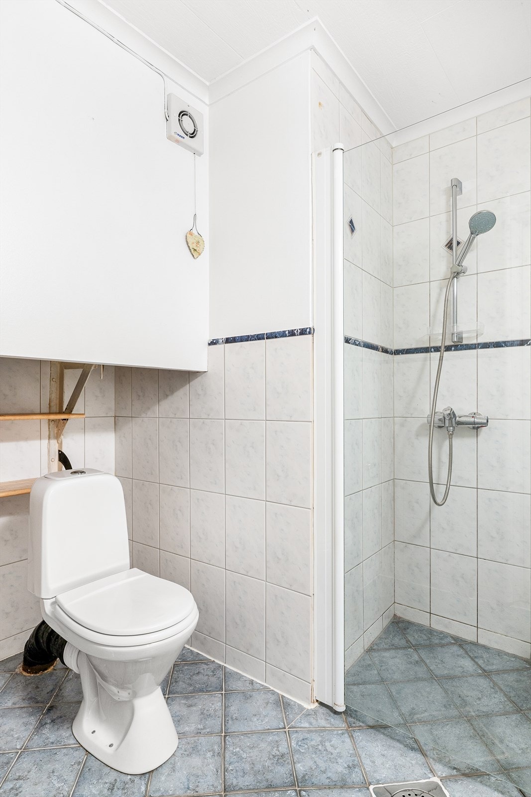 Badet er innredet med dusj på gulv med dører i glass, servant med underskap og gulvmontert toalett. Galleribilde