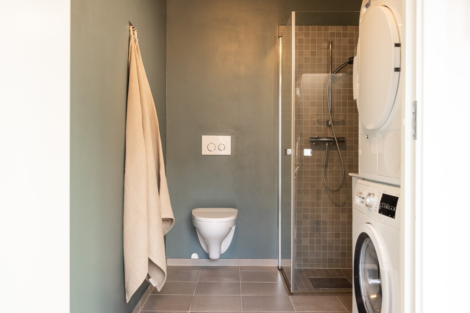 Pent baderom med 90x90 dusjnisje, baderomsinnredning med speil, vegghengt toalett og opplegg for vaskemaskin og tørketrommel. Galleribilde