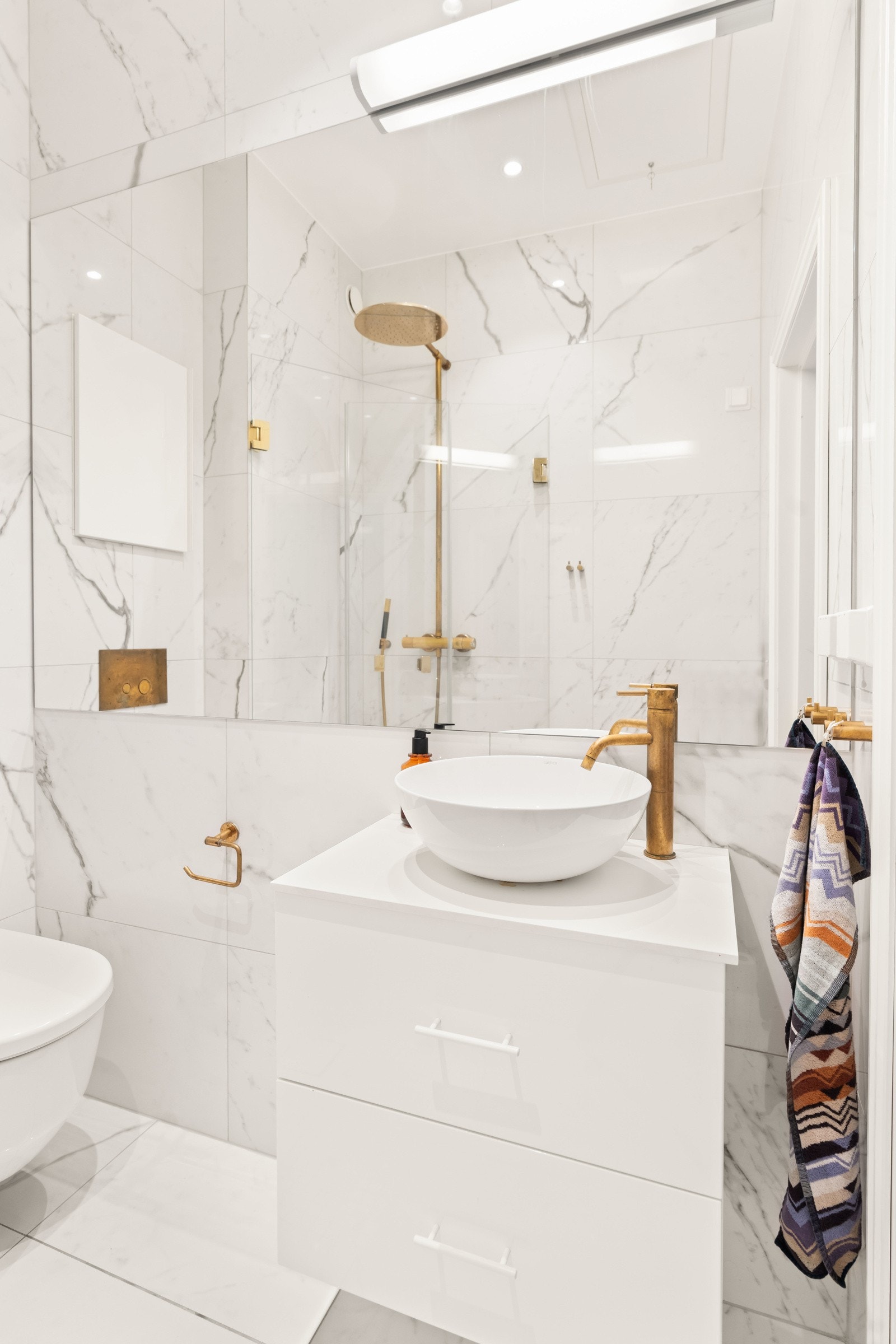 Badet består av vegghengt toalett, servant med servantskap og stort speil langs hele veggen, dusjhjørne med to svingbare glassdører og opplegg for vaskemaskin. Galleribilde