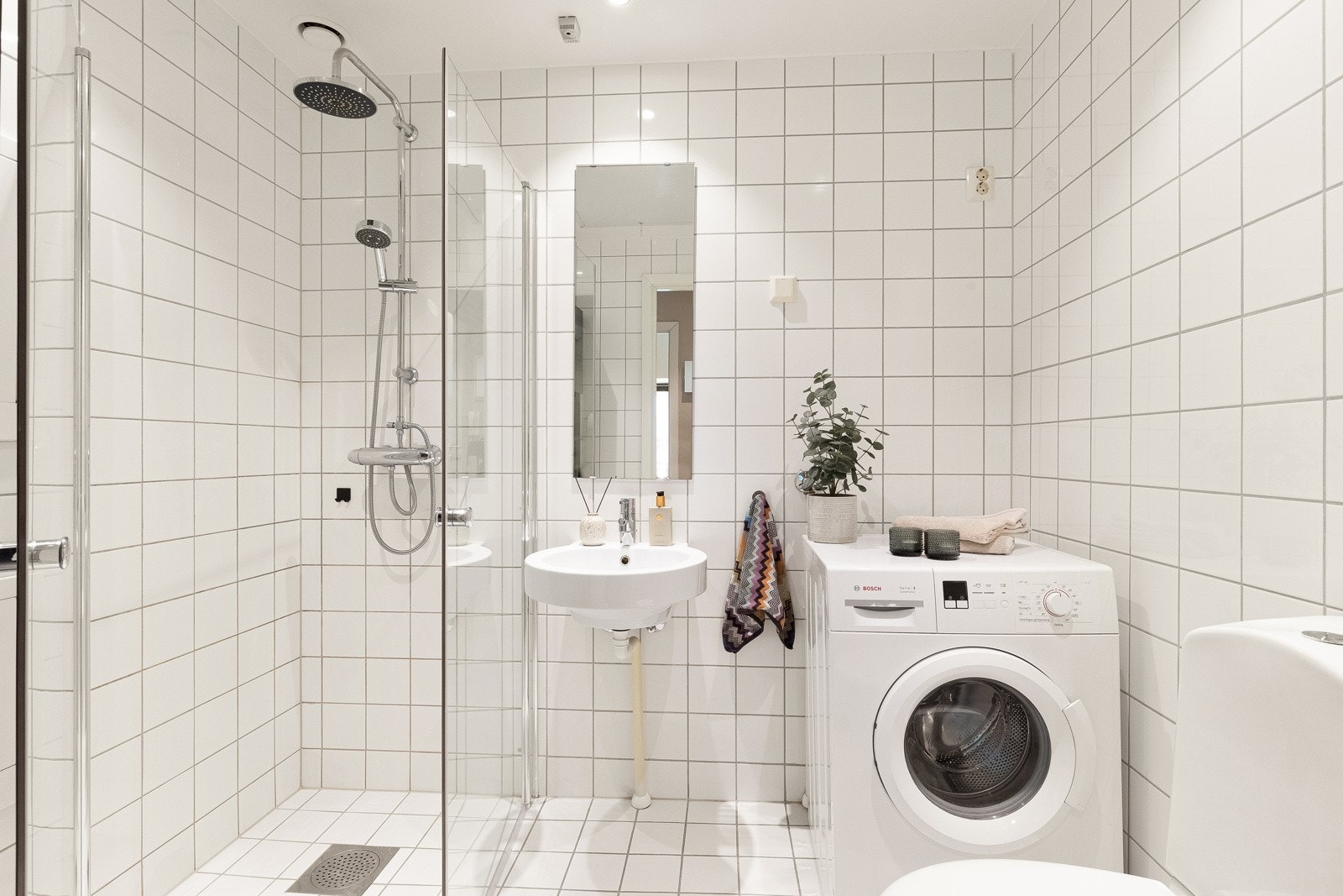 Flislagt, tidløst baderom som inneholder dusjhjørne, servant, toalett og opplegg for vaskemaskin. Galleribilde