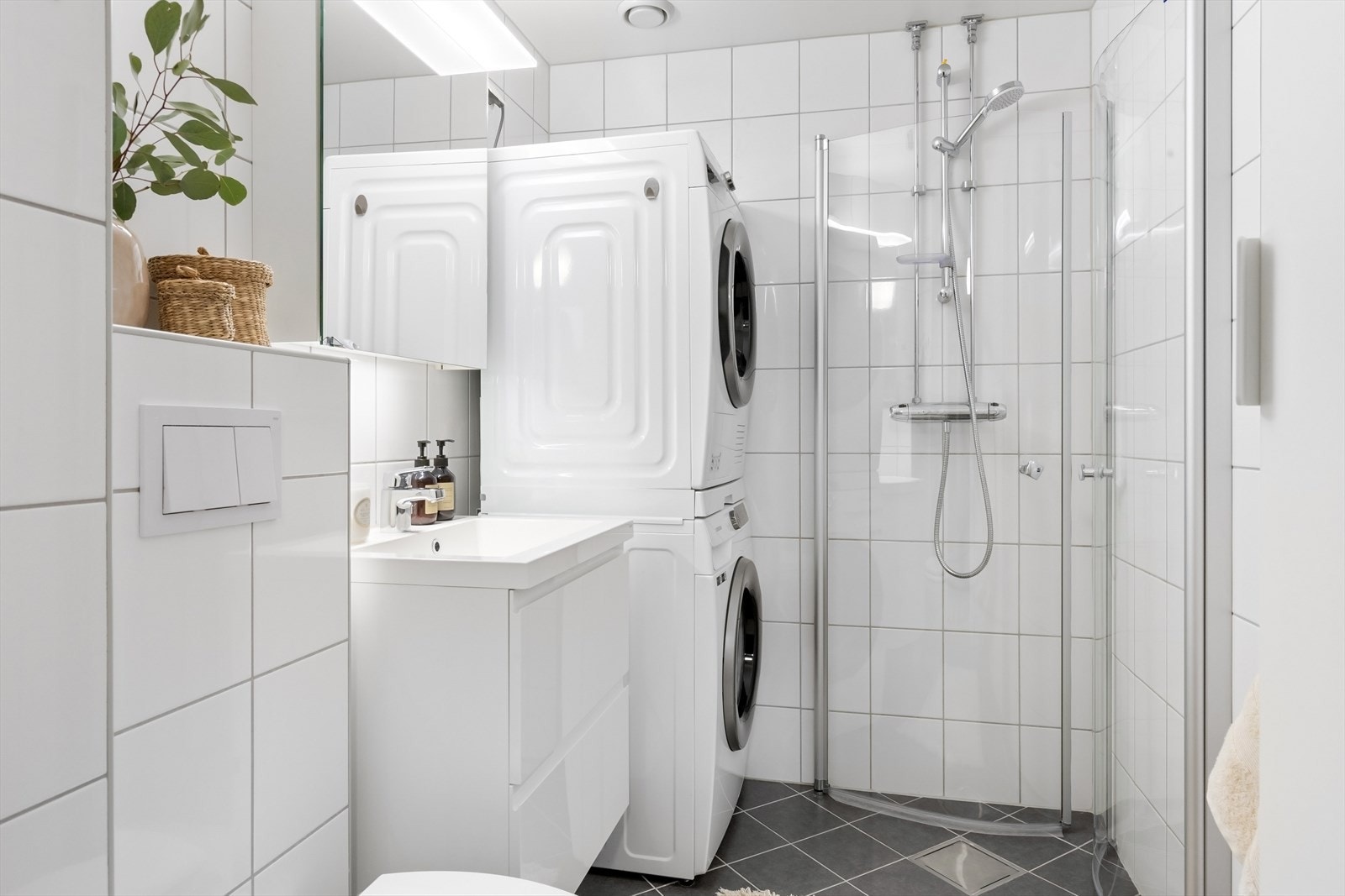 Pent bad med hjørnedusj, innsvingbare glassdører, servant med skuffer, speilskap og vegghengt toalett. Galleribilde