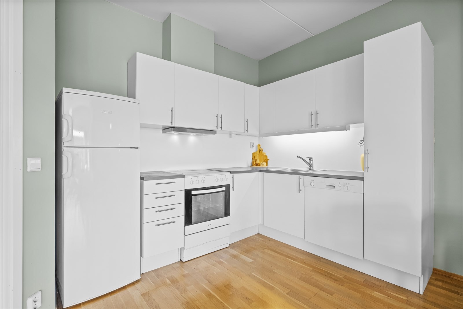 Kjøkkeninnredning med glatte fronter og foliert benkeplate. Kjøkkenet er utstyrt med komfyr, kum med ettgreps blandebatteri, ventilator, kjøl/fryseskap, ovn og oppvaskmaskin. Galleribilde