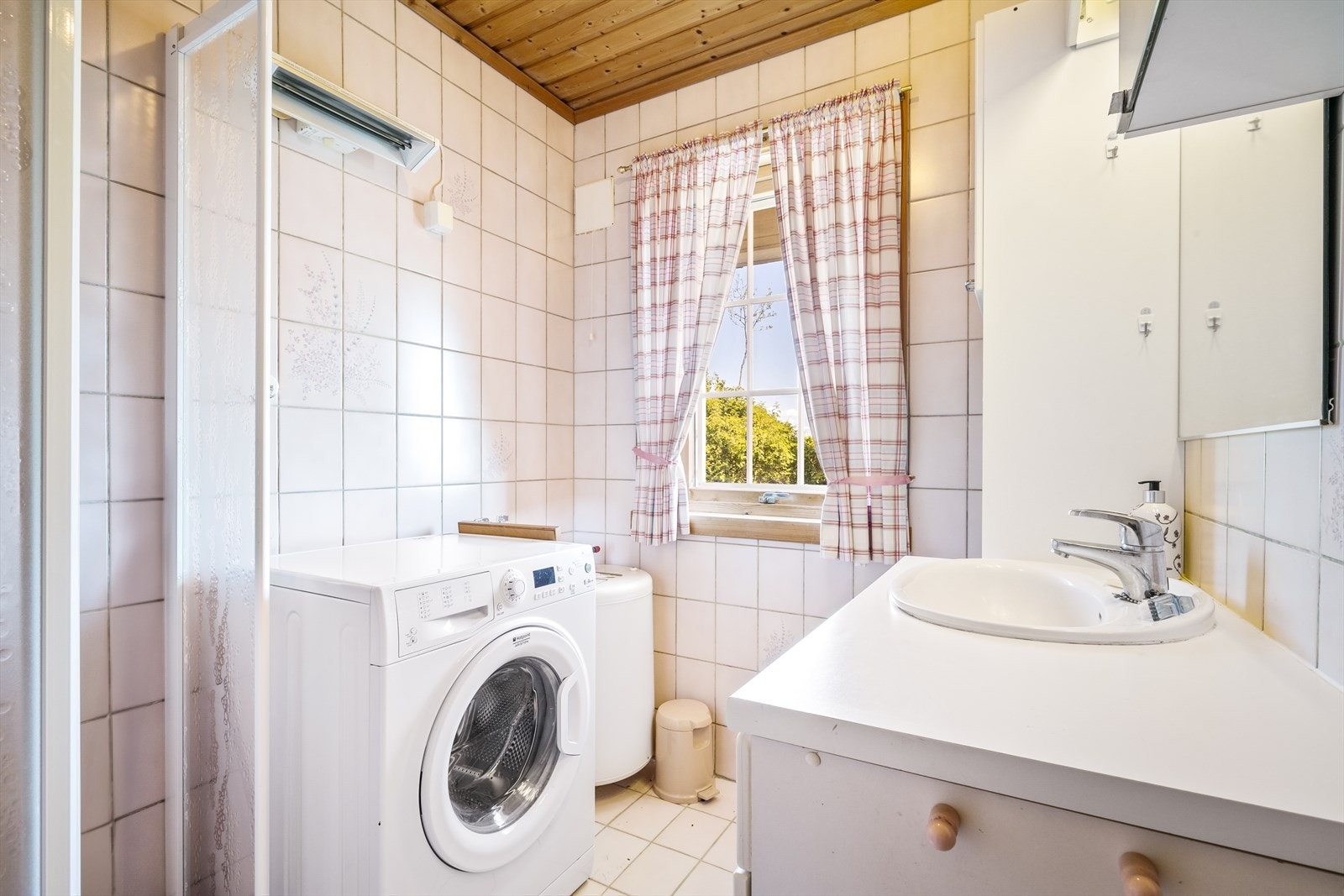 Badet er lyst og inneholder helstøpt servant, skap under servant med slette fronter, dusjdører i klart glass, opplegg for vaskemaskin og varmtvannsbereder. Galleribilde