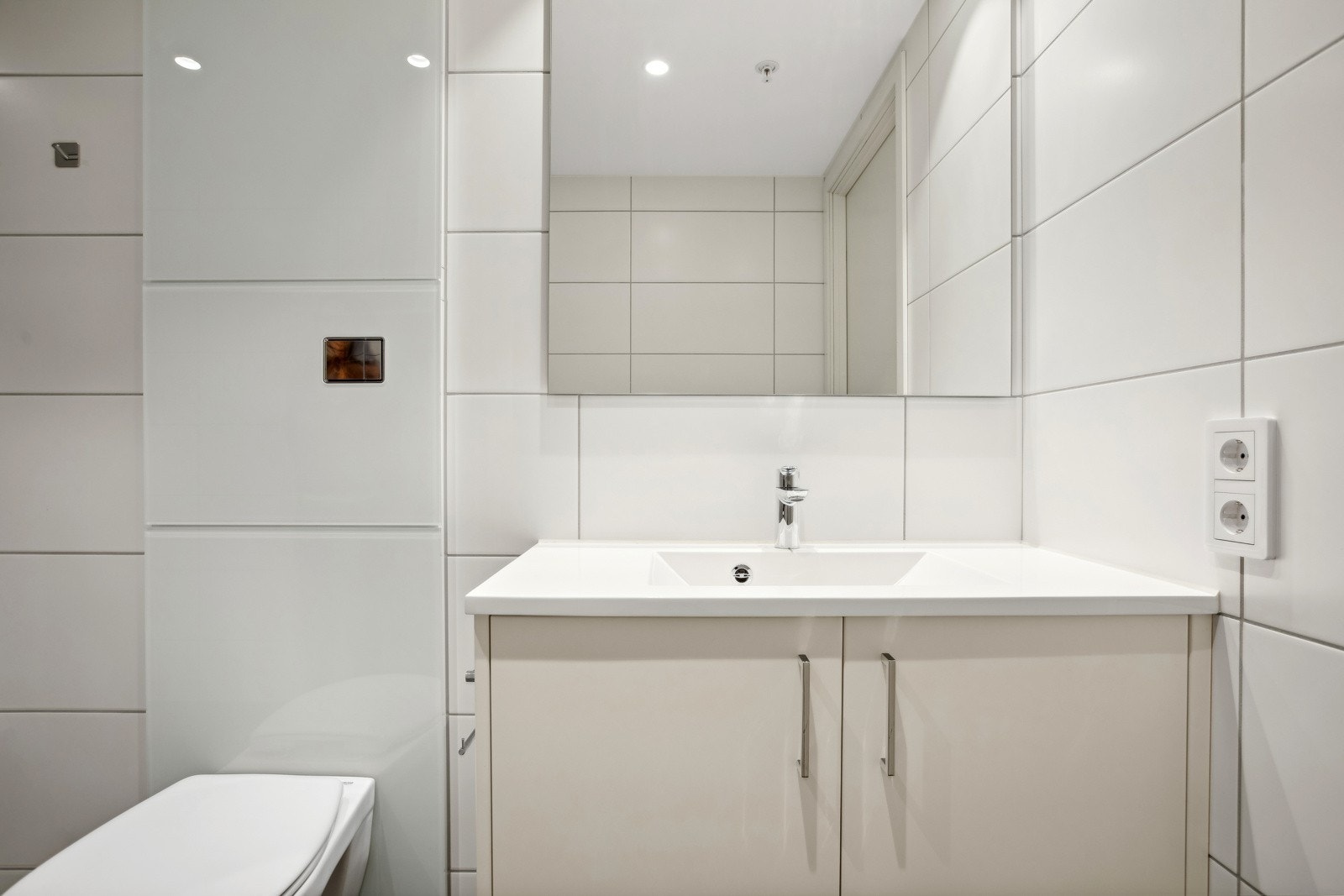 Badet har lys innredning med servant, speil, veggmontert toalett, dusjhjørne og opplegg for vaskemaskin og tørketrommel. Galleribilde