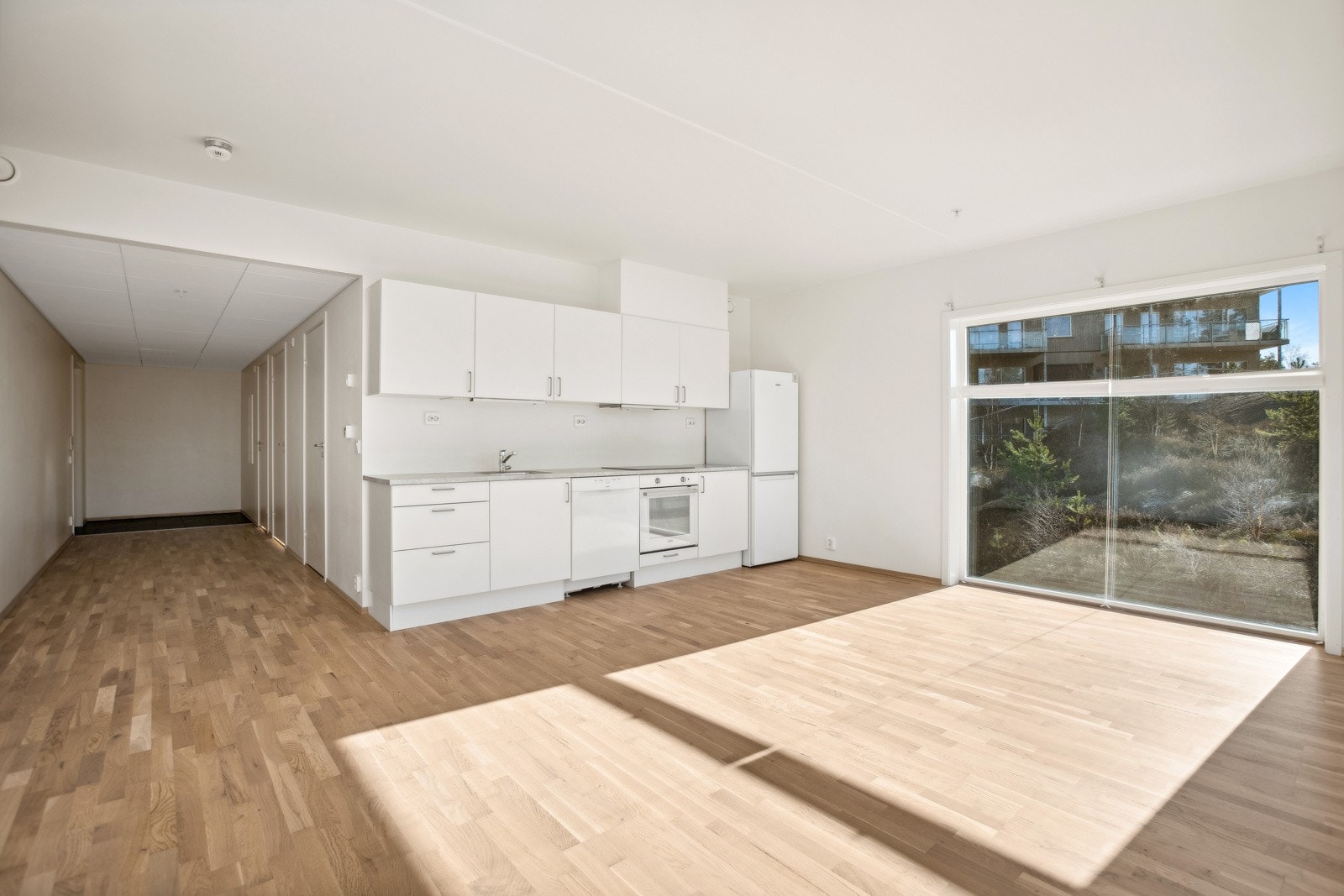 Lys kjøkkeninnredning med glatte fronter, benkeplater i laminat, oppvaskkum med ett-greps blandebatteri og ventilator over kokesonen. Galleribilde