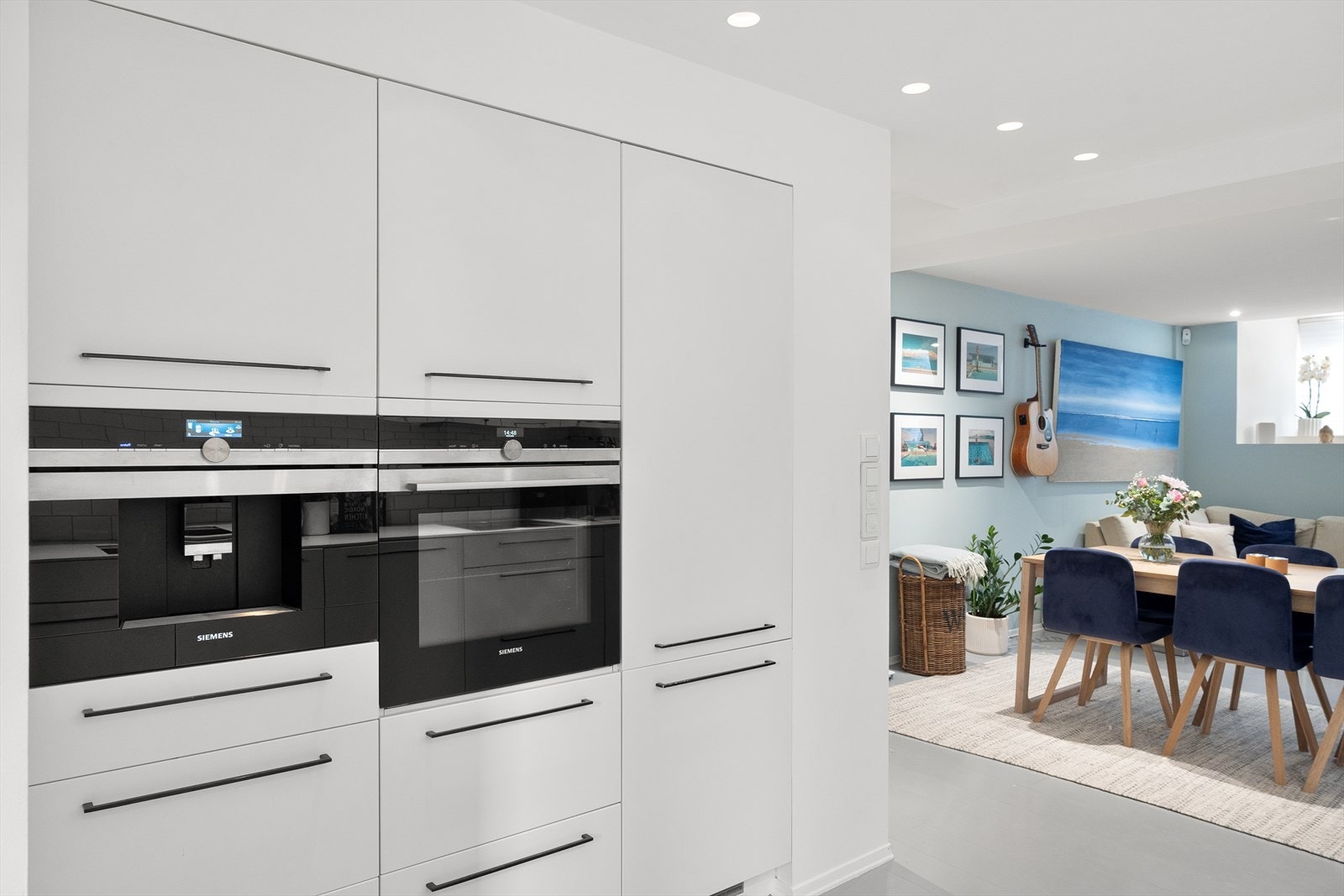 Kjøkkenet ligger i åpen løsning mot stuen og er utstyrt med integrerte hvitevarer, inkludert komfyr med platetopp, oppvaskmaskin, kaffemaskin og kjøl/frys Galleribilde