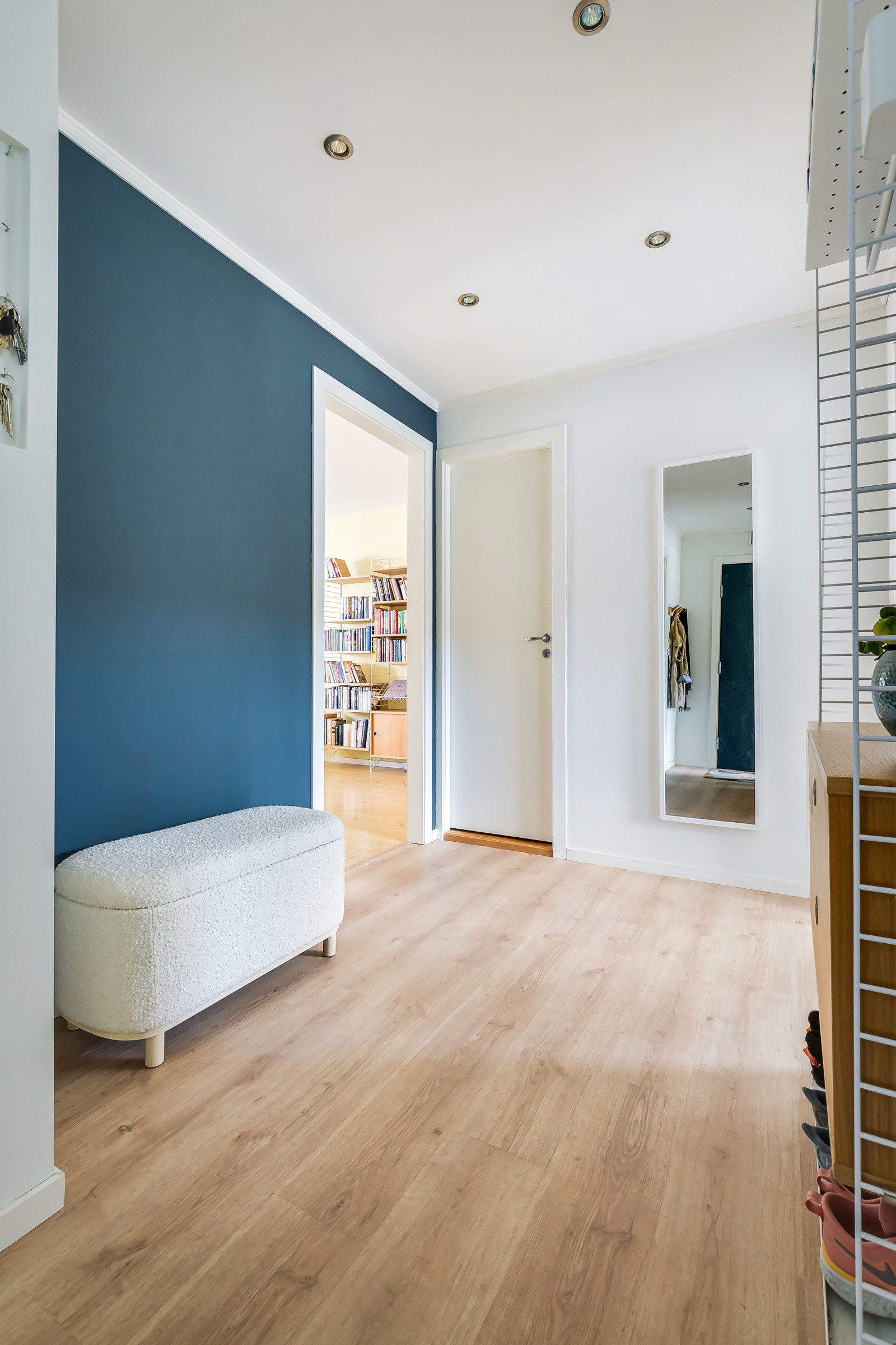 Du ønskes velkommen inn i en lys, fin og romslig entré. Moderne standard med pen enstavs laminat fra 2023 på gulv, glatte lysmalte overflater med en blå kontrastvegg og downlights i himlingen. Galleribilde