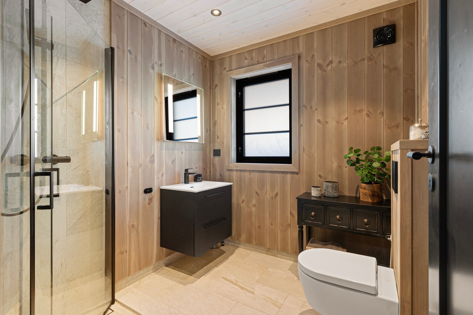 Hytta har 2 lekre bad. Hovedbadet har tilkomst fra gang i 1.etg. Badet inneholder dusjhjørne med regnfall-armatur og tile-in sluk, innredning med servant og veggmontert toalett. Flislagt gulv med varmekabler Galleribilde