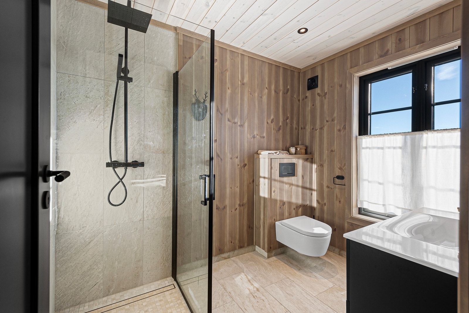 Baderom 2 med tilkomst fra hovedsoverom. Baderommet inneholder dusjhjørne med glassdører, regnfall-armatur og tile-in sluk. Innredning med skuffer og nedfelt servant samt veggmontert toalett Galleribilde