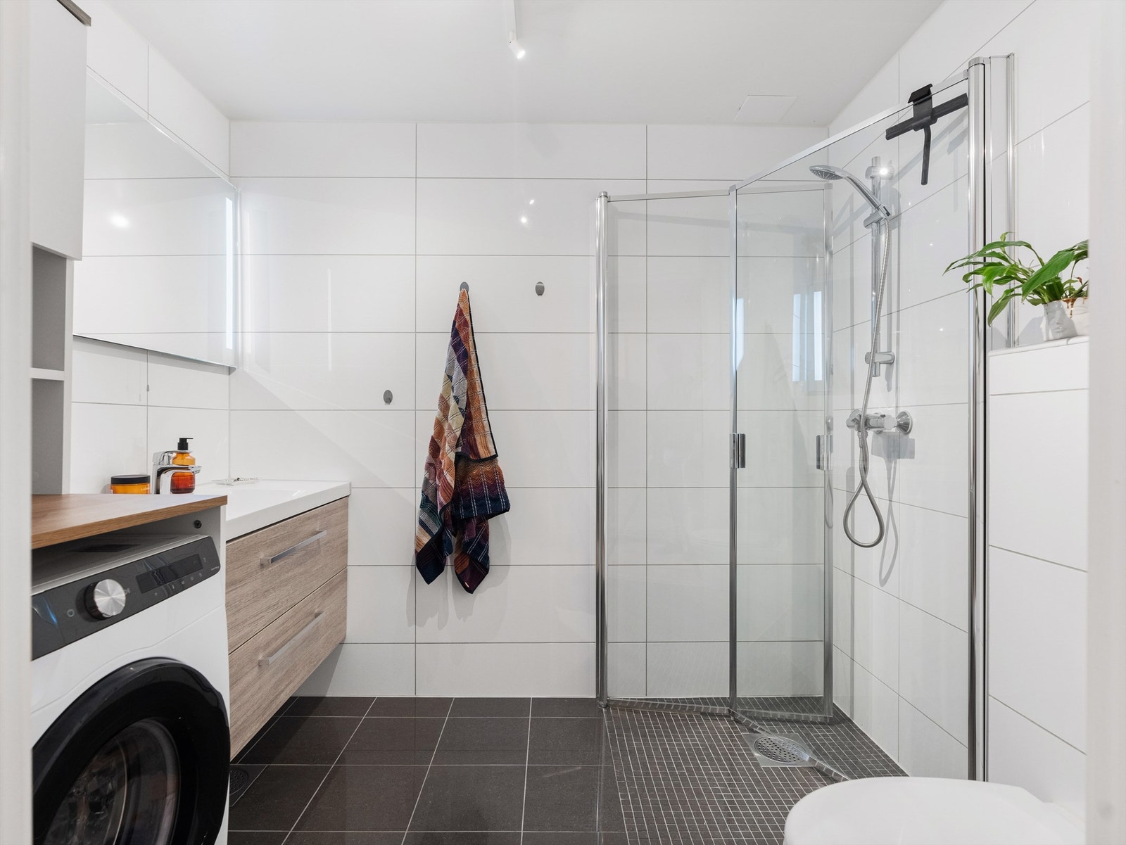 Badet har flislagte vegger og gulv, utstyrt med vegghengt toalett og servantskuff. Dusjhjørnet har innfellbare glassdører Galleribilde