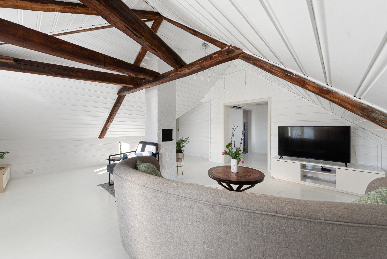 Skråtak gir rommet karakter, mens hvite vegger og gulv skaper en følelse av romslighet. Rommet har åpen løsning mot et tilstøtende rom med spiseplass. Galleribilde