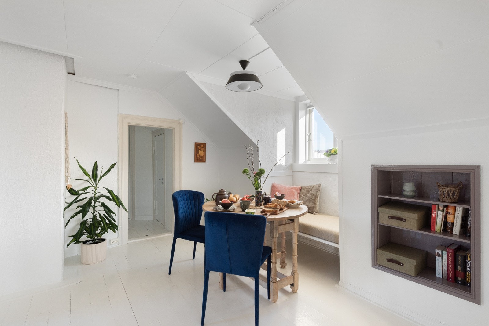 Lys og koselig spiseplass med skråtak, innebygd bokhylle og hvitmalte vegger. Store vinduer gir godt med naturlig lys. Galleribilde