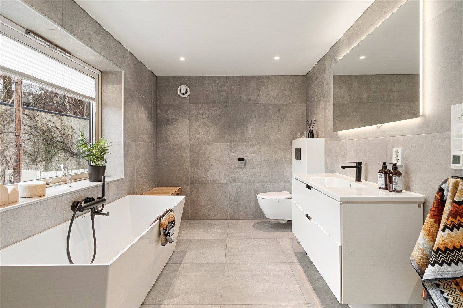 Badet er utstyrt med dusj, badekar, veggmontert wc, servant med skap og spegel. Galleribilde