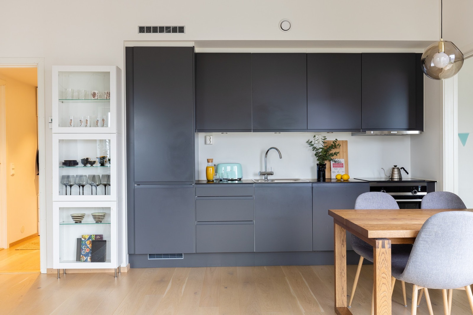 Pent Sigdal kjøkken med grå, fabrikklakkerte fronter og takhøyde overskap. Benkeplate i kompakt laminat med nedfelt oppvaskkum og nedfelt induksjon koketopp. Galleribilde