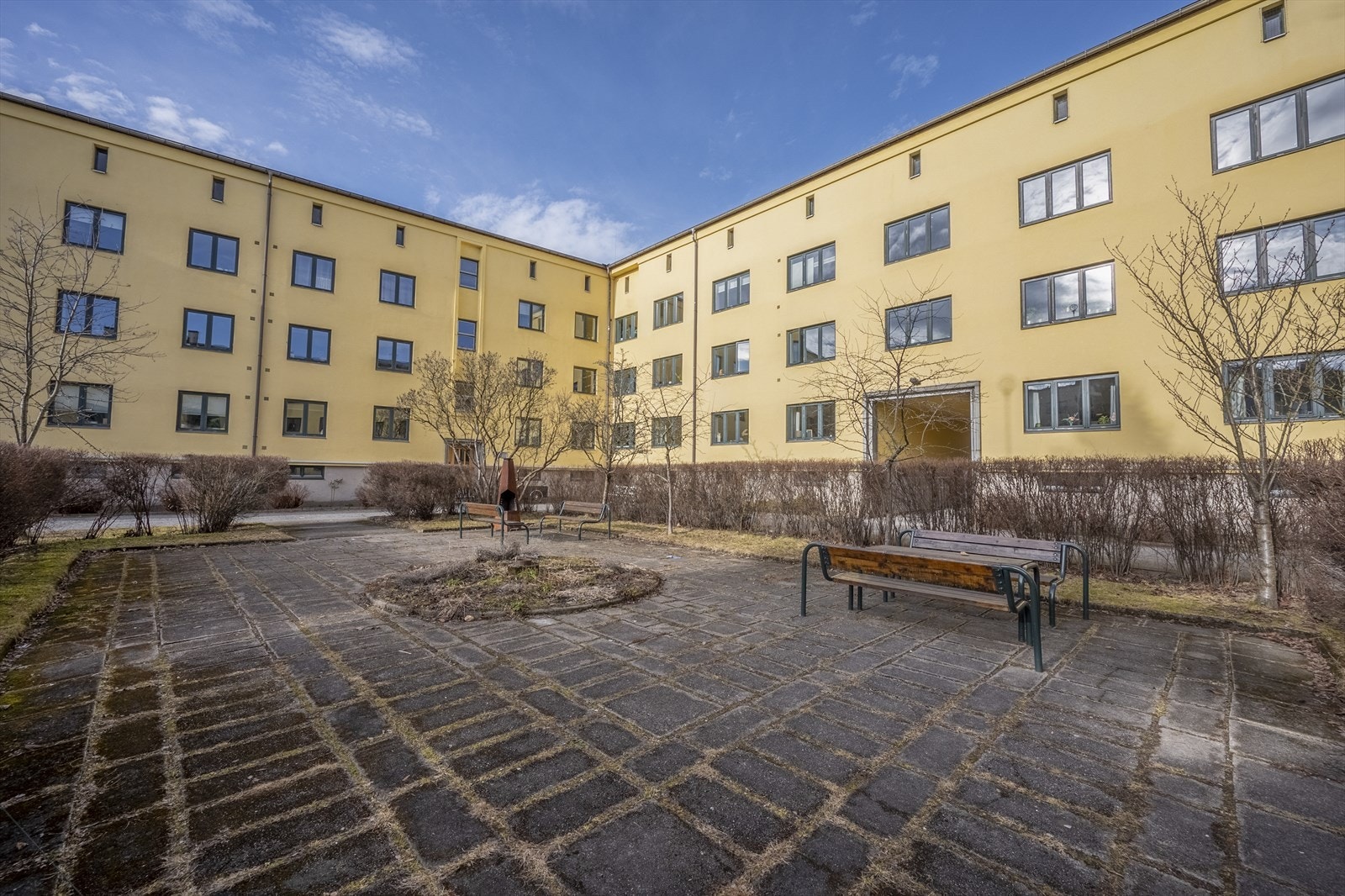 Hyggelig bakgård med flere sittegrupper og frodige busker og trær om våren/sommeren. Galleribilde