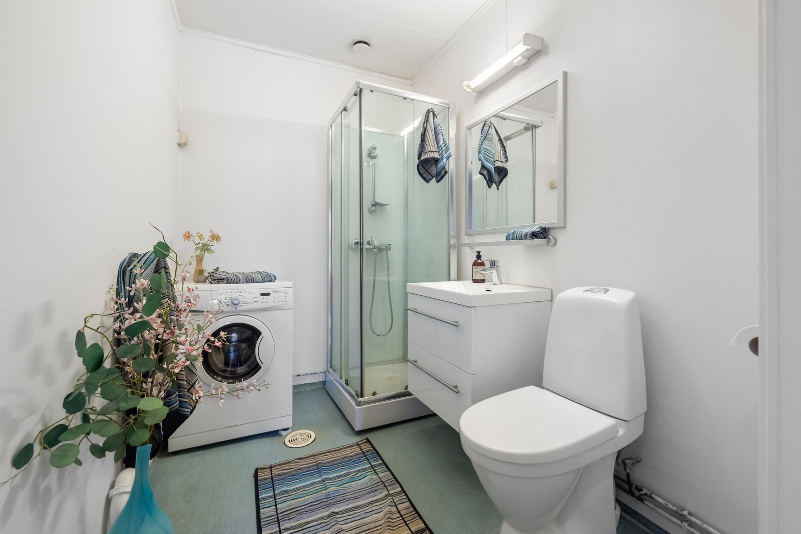 Baderommet er innredet med vegghengt servantskap med glatte fronter, vegghengt speil med overbelysning, dusjkabinett med skyvedører og dusjarmatur tilkoblet hånddusj, og gulvstående toalett. Galleribilde