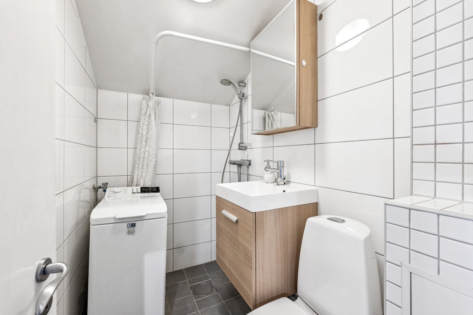 Flislagt bad i regi av borettslaget i 2009. Baderomsinnredningen er bestående av servant med underskap, speilskap, gulvmontert klosett, åpen dusjløsning og opplegg for vaskemaskin. Galleribilde