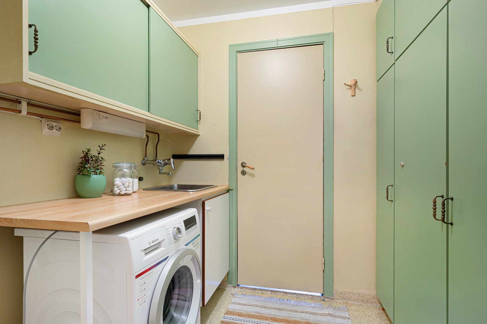 Vaskerom med kran og avløp for vaskemaskin, samt direkte inngang til kjøkkenet. Galleribilde