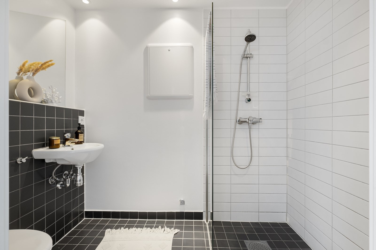 Baderom med flislagt gulv, varmekabler, fliser og malte flater på vegger, avtrekk, speil, downlights, servant, dusj hjørne med glassvegg, vegghengt toalett. Galleribilde