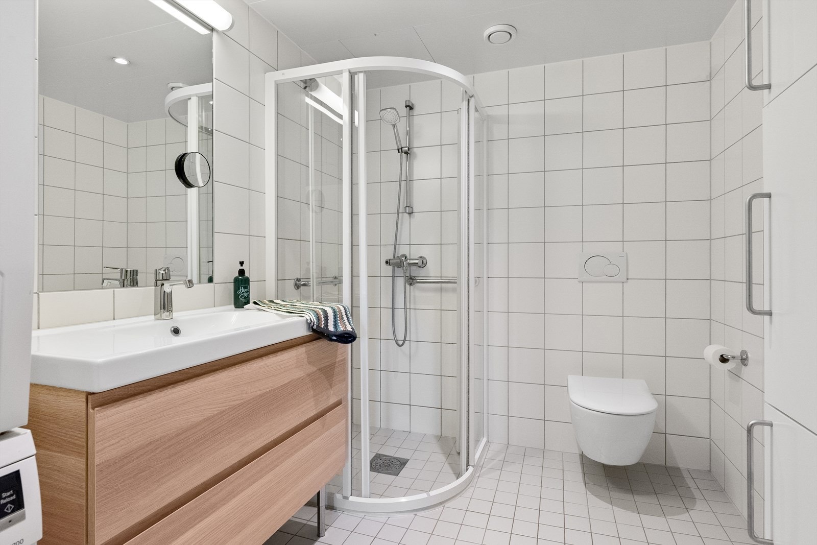 Nyere vegghengt toalett, dusjvegger i klart glass og speil over servant. Opplegg for vaskemaskin og tørketrommel. Nyere baderomsinnredning med mye skapplass. Galleribilde