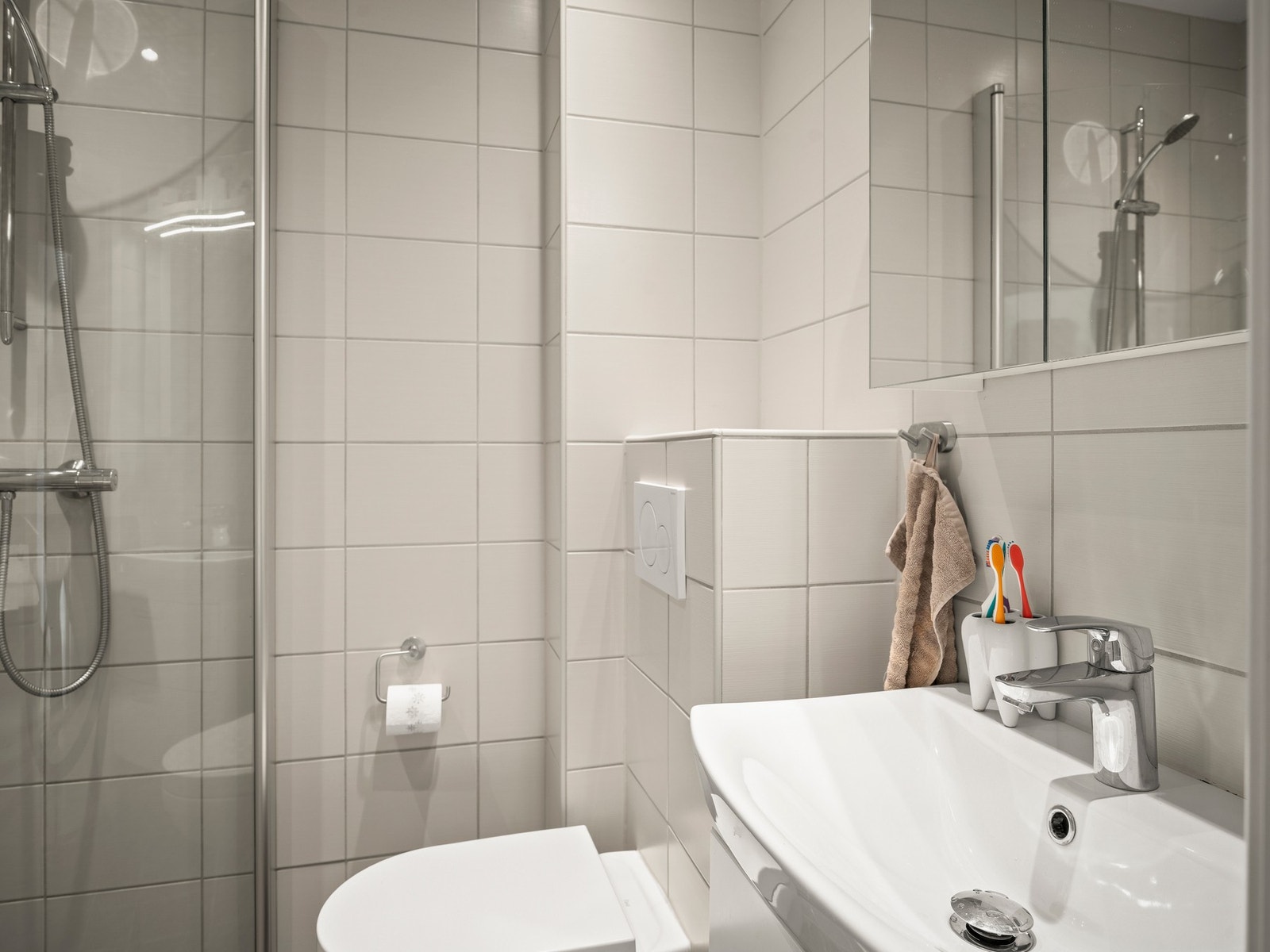 Badet er utstyrt med dusj med innfellbare glassvegger, servantseksjon med skuffer og heldekkende porselensvask, speilskap med lys, vegghengt wc og opplegg for vaskemaskin. Galleribilde