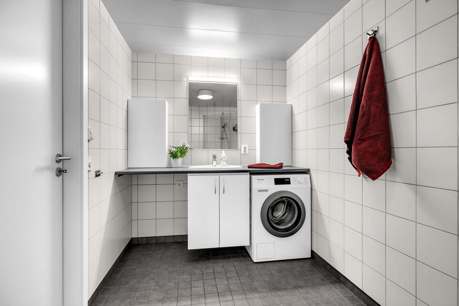 Lyst bad med flislagte vegger og flislagt gulv med elektriske varmekabler. Opplegg for vaskemaskin og tørketrommel Galleribilde