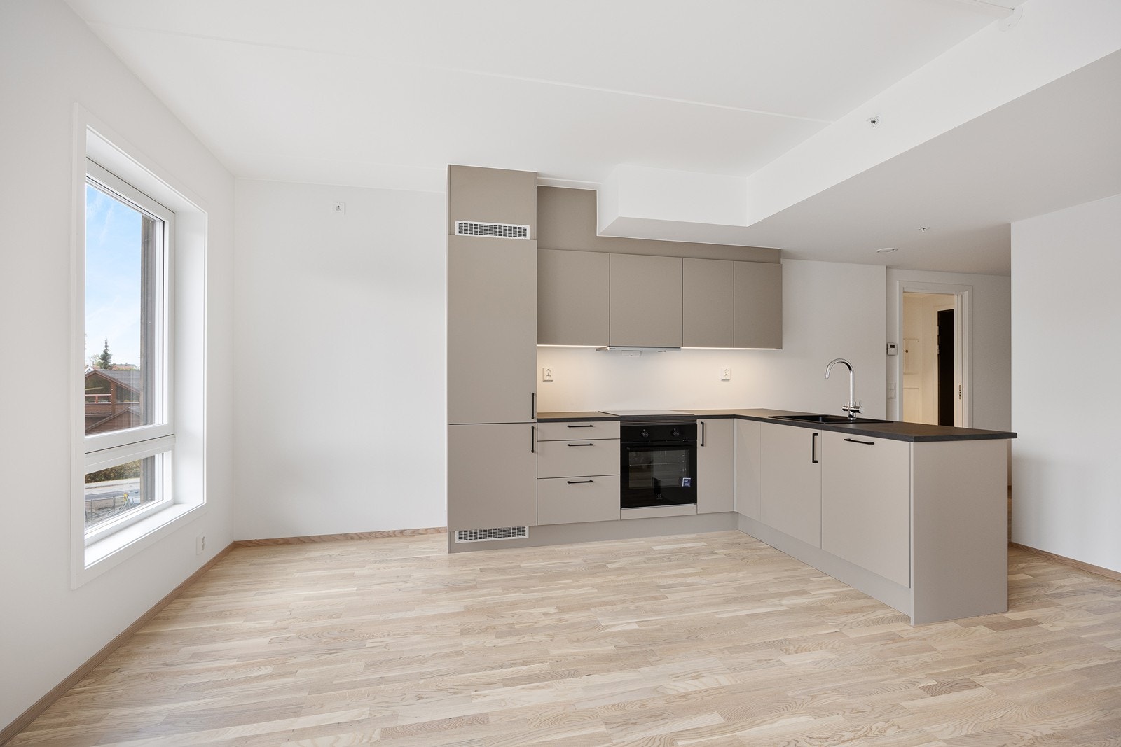 Kjøkkenet er innredet med glatte beige fronter, sorte håndtak og mørk laminat benkeplate. Galleribilde