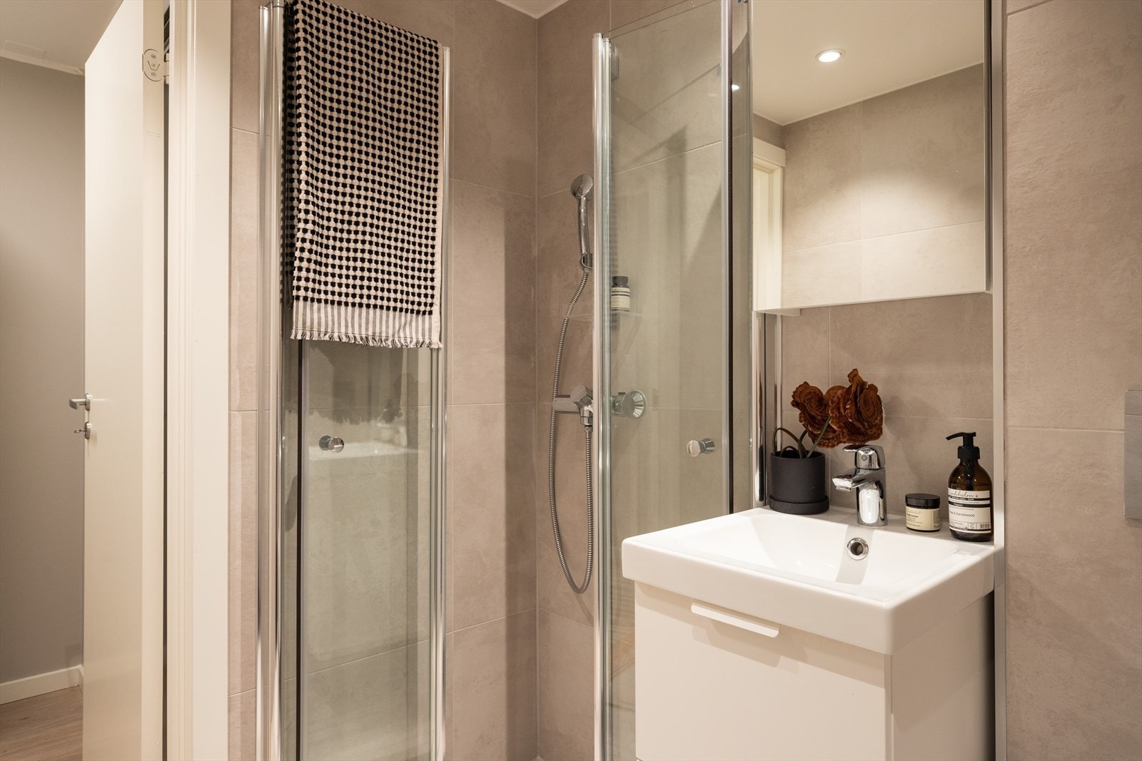 Badet er utstyrt med avtrekk, speilskap, downlights, servant med innredning, dusj hjørne med innfellbare glassdører og vegghengt toalett Galleribilde