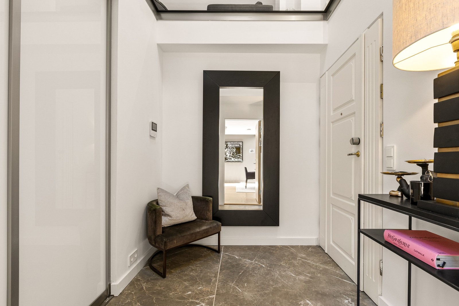 En stilren skyvedørsgarderobe gir praktisk og effektiv oppbevaring av yttertøy og sko, mens det flislagte gulvet med gulvvarme sørger for både eleganse og komfort. Galleribilde