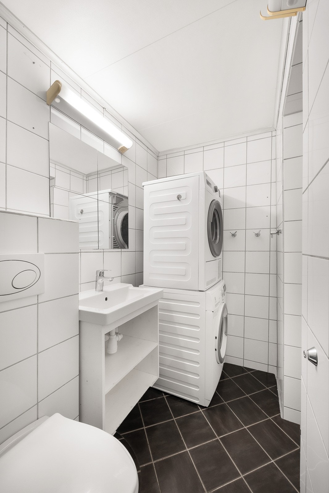 Innredningen består av servant på hvit hylle, speil med belysning og et gulvmontert toalett. Galleribilde