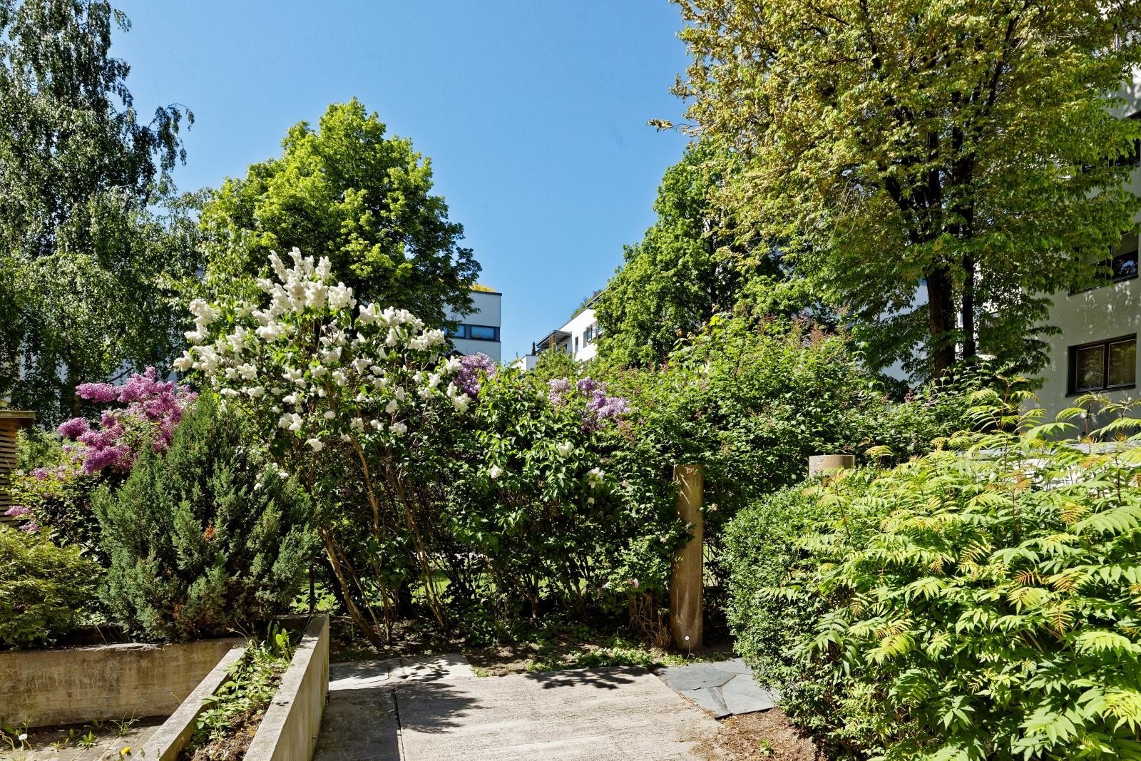 Tomten er pen og opparbeidet med betong- og steinsatte arealer, belegningsstein, variert beplantning, gressplener, lekeapparater og sittegrupper Galleribilde