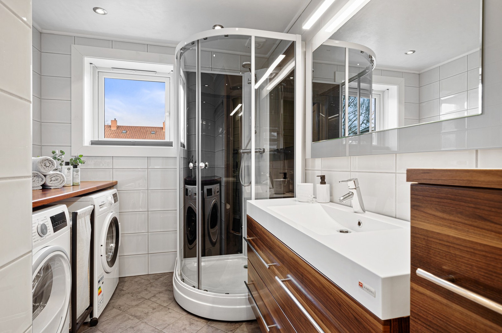 Pent flislagt bad med dusjkabinett, vegghengt toalett, romslig servantskuffe til oppbevaring og kran og avløp til vaskemaskin. Galleribilde