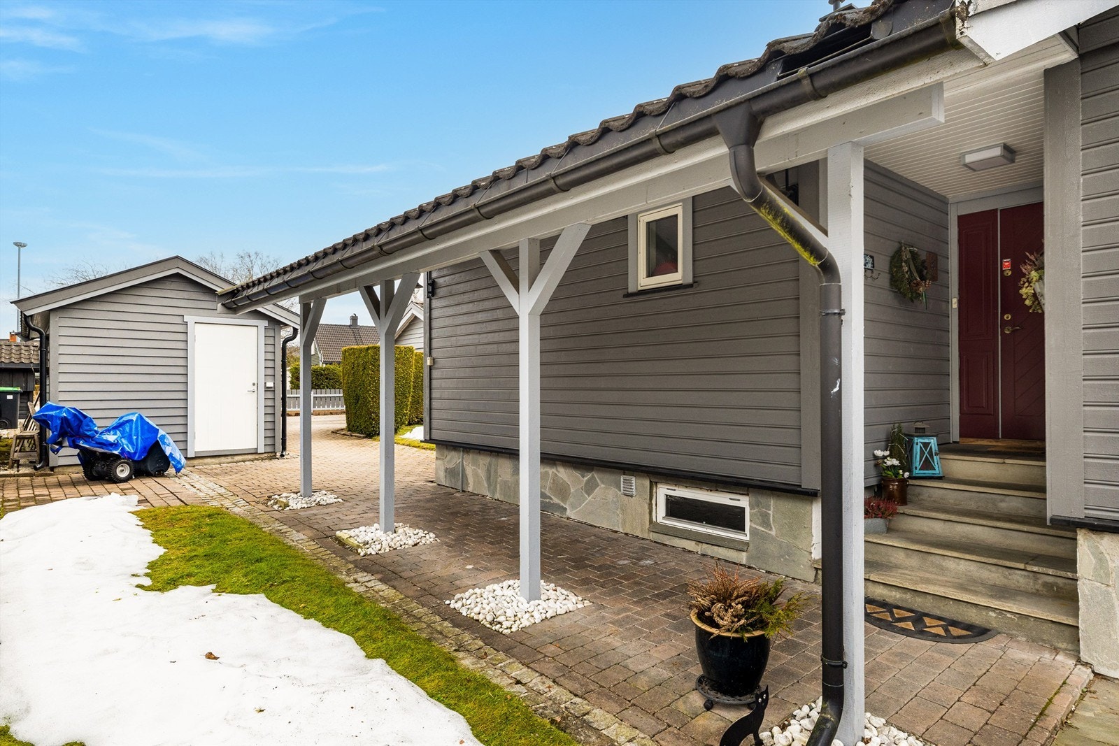 Gjennomført med belegningsstein i gårdsplass og inngangsparti. Rullestein ved søylene til takoverbygget og skiferlagt trapp. Galleribilde