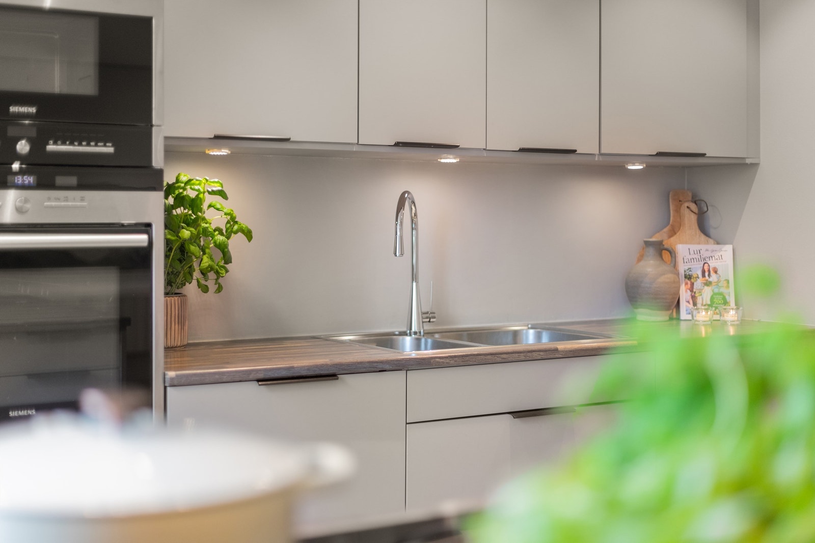 Nedfelt oppvaskkum i rustfritt stål med ett-greps armatur og belysning mellom benkeplate og overskap. Galleribilde