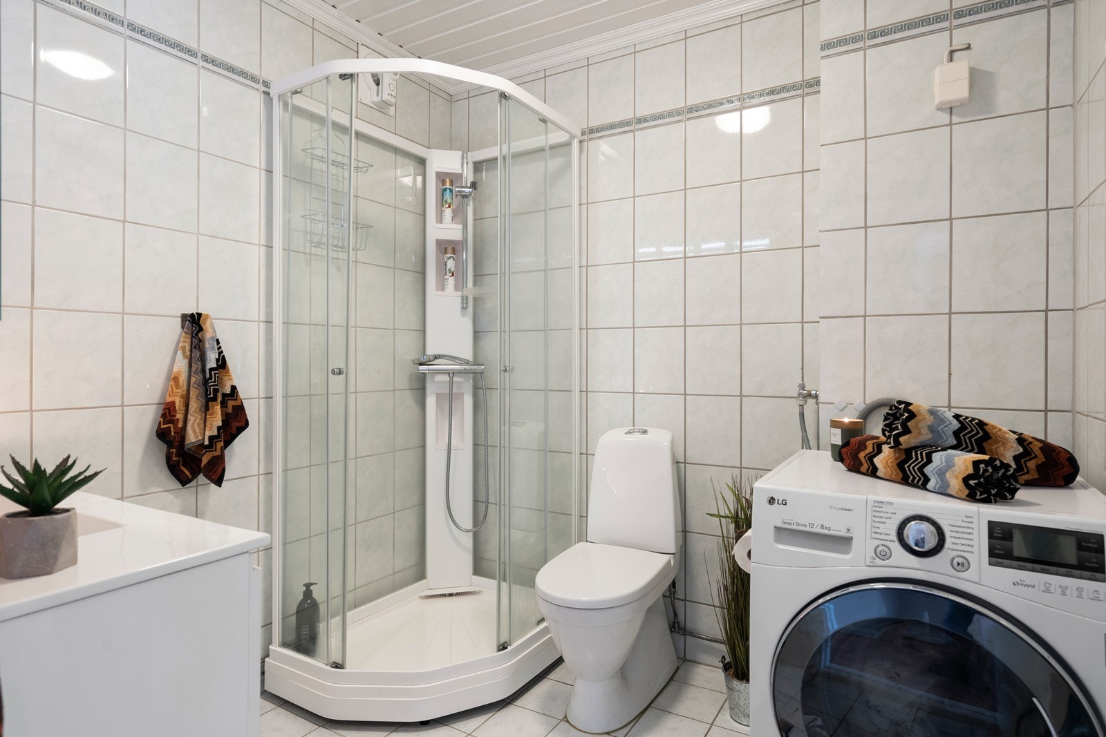 Bad med dusjhjørne, gulvmontert wc og opplegg for vaskemaskin Galleribilde