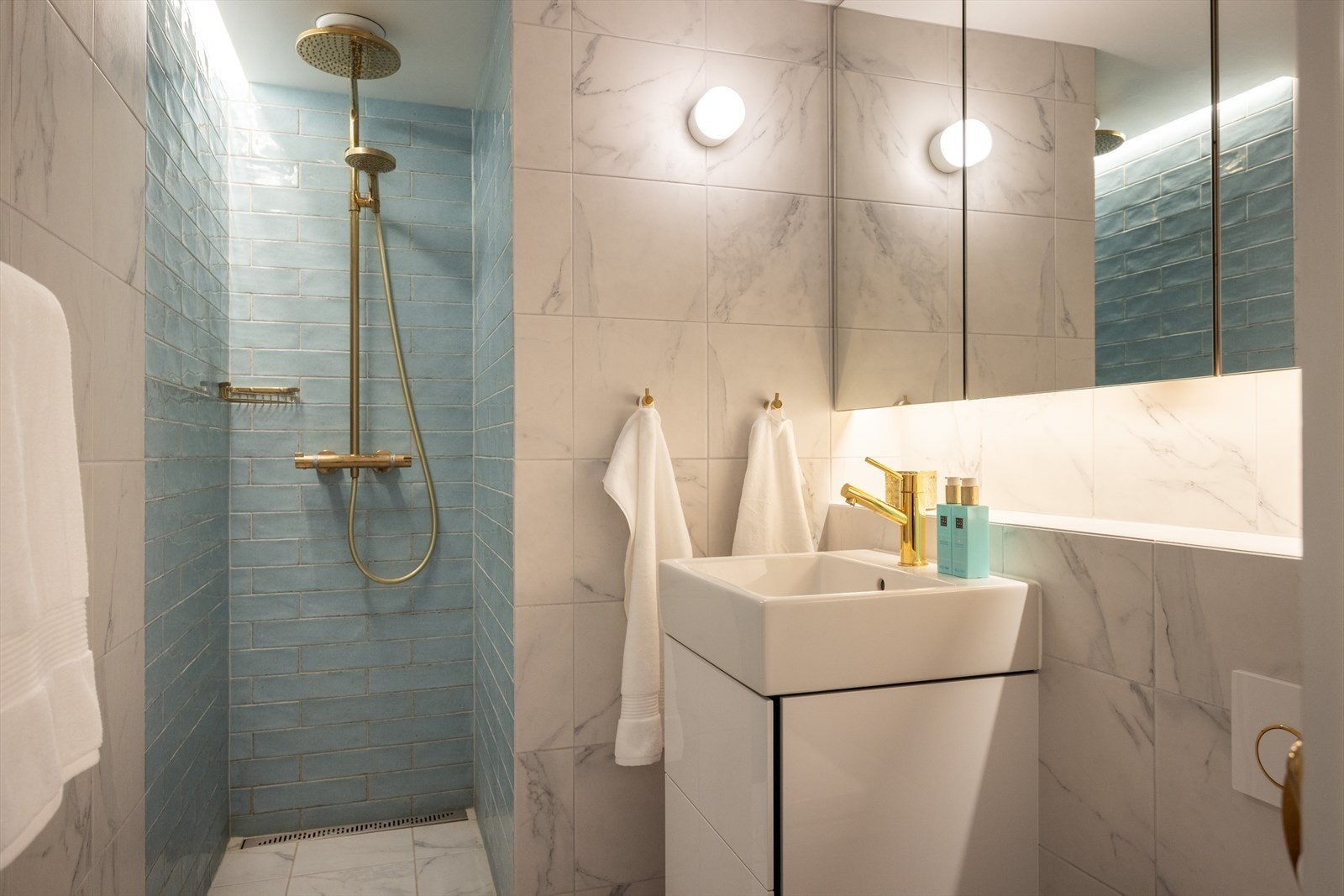 Badet har en flislagt dusjnisje med spennende fargekombinasjoner som komplementerer armaturene og de elegante detaljene i messing Galleribilde