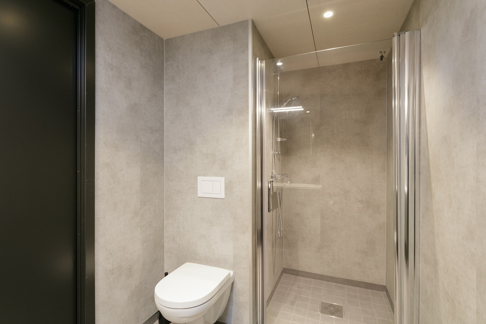 Dusjhjørne med glassvegg og vegghengt dusjarmatur. Vegghengt toalett. Galleribilde