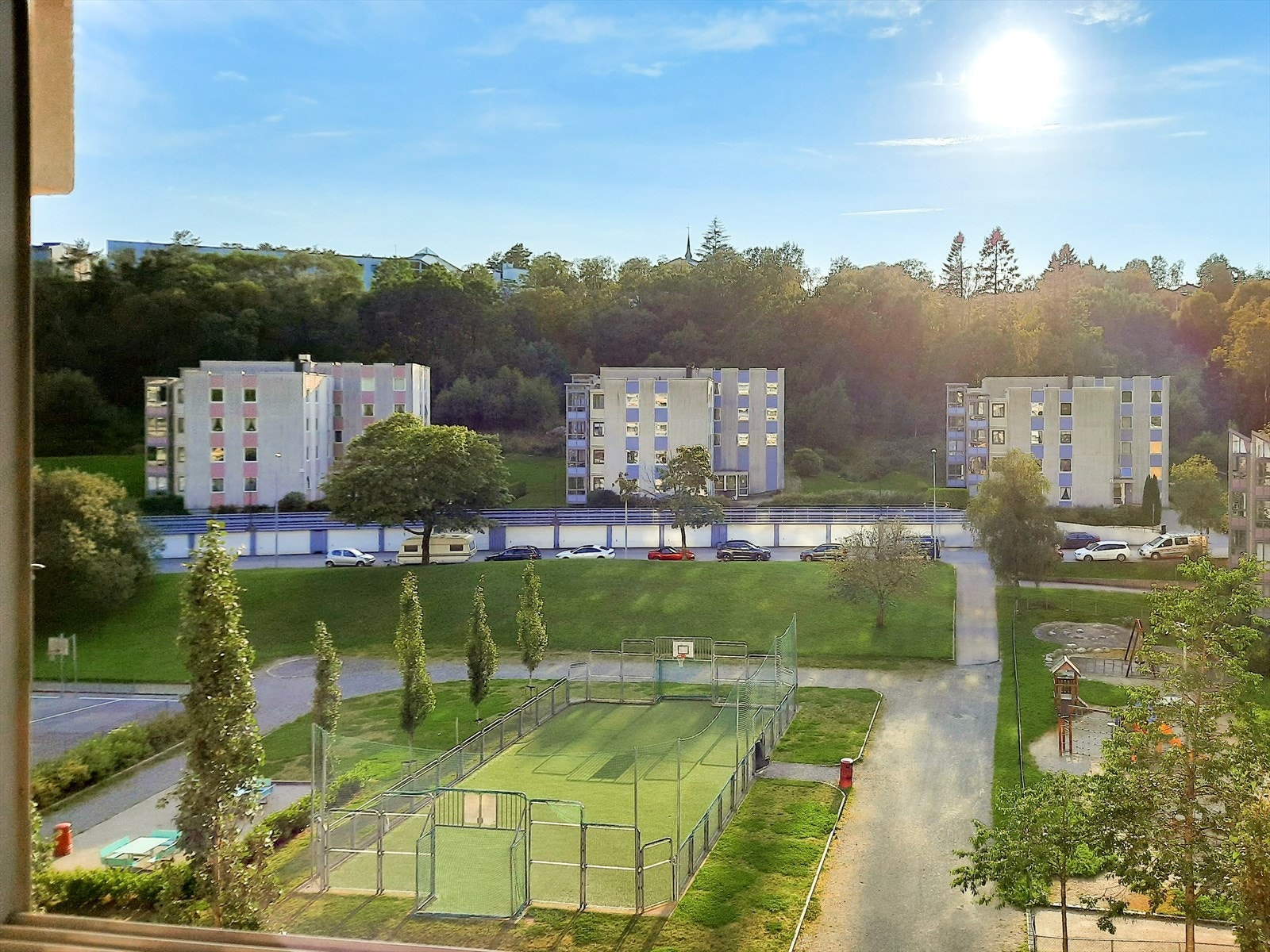 Solrik beliggenhet med utsikt over grønne omgivelser, boligblokk og nærhet til lekeplass og fotballbane. Galleribilde