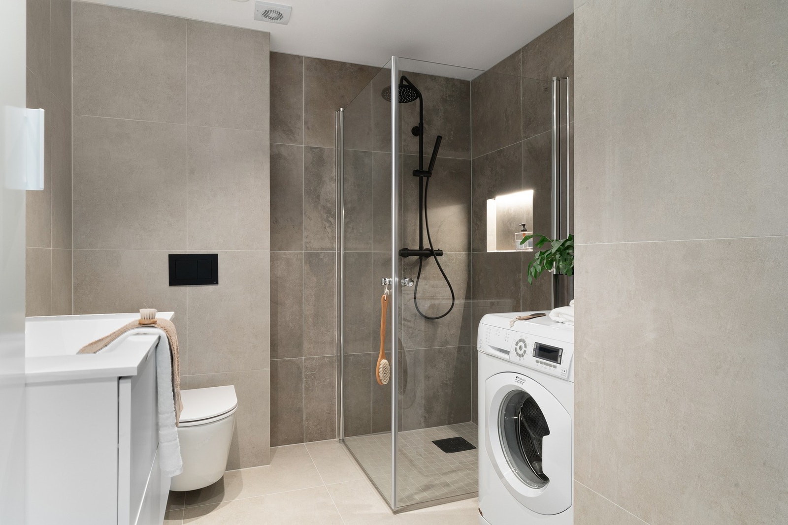 Badet er innredet med toalett, dusj med glassvegger baderomsinnredning og opplegg for vaskemaskin. Galleribilde